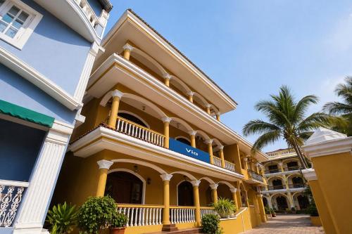 a yellow building with a balcony and palm trees at Via Romeo's Stay - A Beach Property in Baga
