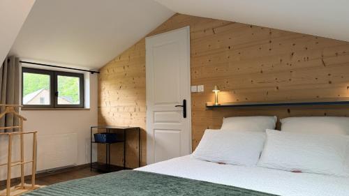a bedroom with a white bed and a wooden wall at Ferme du Bien Hêtre Gîte Cosy in Saint-Arnoult