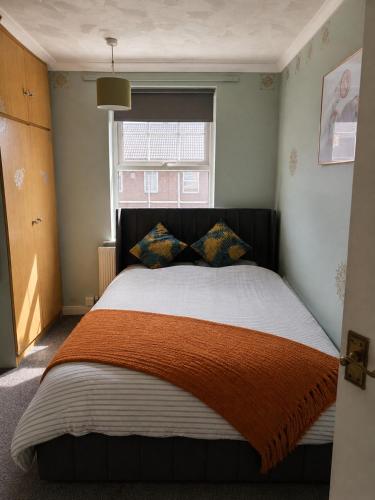 a bedroom with a bed with an orange blanket and a window at The Grimsby Heneage Stay in Grimsby