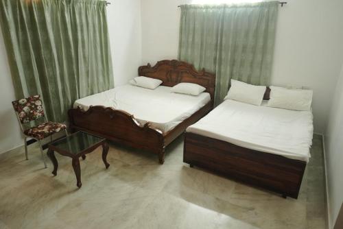 two beds in a room with a chair and a table at Pulimada Stays in Trichūr