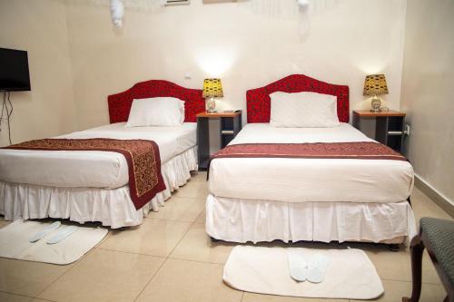 two beds in a hotel room with red headboards at St Augustine Apart & Hotel in Kigali