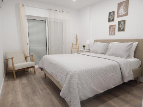 a white bedroom with a large bed and a chair at Casa Bella Arch, 2 min walk to beach Praia da Rocha in Portimão