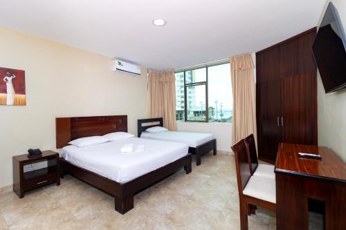 a bedroom with two beds and a desk and a television at Hotel Marvento Suites in Salinas