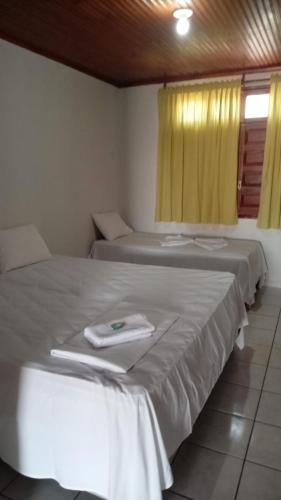 two beds in a room with yellow curtains at Carranca Grande Hotel in Xique-Xique