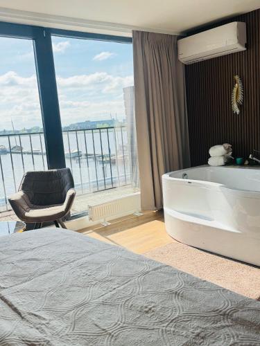 a bedroom with a tub and a chair and a large window at Weromerie Premium Hotel and Apartment in Wormer