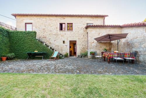 a stone house with a table and an umbrella at Casa Justininho in Ponte de Lima