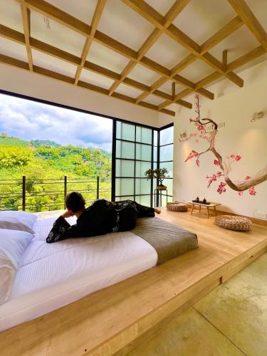a man laying on a bed in a room with a large window at Glamping Raíces in Manizales