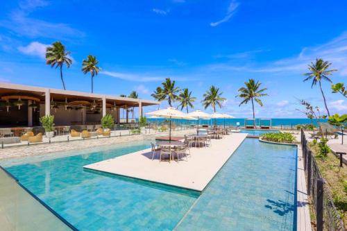 a resort pool with tables and umbrellas and the ocean at Resort Cais Eco Residence in Ipojuca