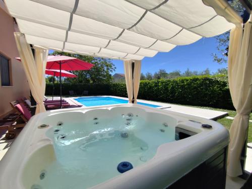 a jacuzzi tub under an umbrella next to a pool at Villa Tramonto 4 stars, Krnica in Krnica