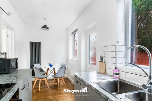 a white kitchen with a sink and a table at Spacious 2BR Home w Garden 2-Min Walk to Town in Stockport