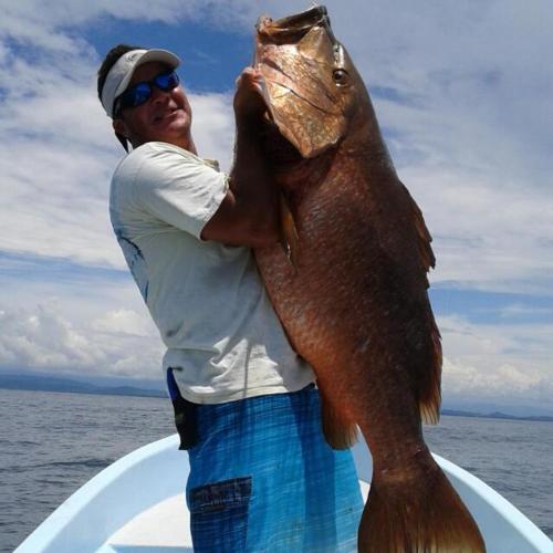 a man standing on a boat holding a large fish at Banana Bay Marina in Golfito