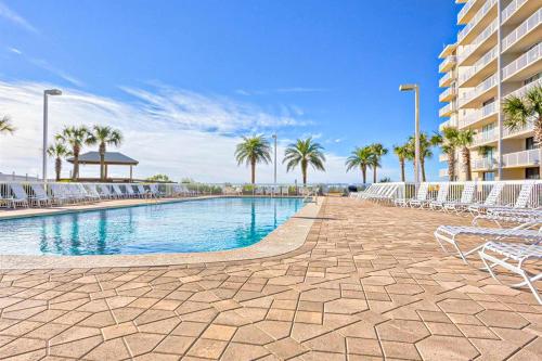 a swimming pool with chairs and palm trees and a building at Fantastic condo with elevator WiFi & central AC - beachfront Location in Orange Beach