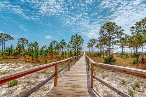 a wooden boardwalk leading to a beach with trees at Bale Oasis in Dauphin Island