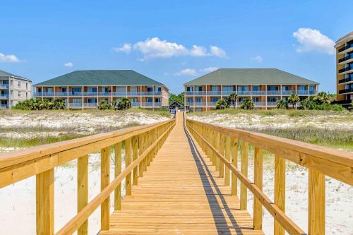 a wooden boardwalk leading to two buildings on the beach at Gulf-Front Condo with Balcony Shared Pools and Beach Access in Dauphin Island