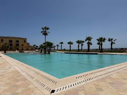 a large swimming pool with palm trees in the background at Fort Chambray Gozo 2BDR Apartment in Għajnsielem