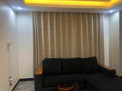 a living room with a black couch in front of a curtain at AJ Space in Kampala