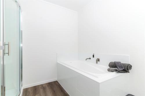 a white bathroom with a sink and a shower at Te Awa Suites in Hamilton