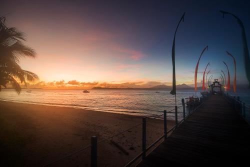 a beach with a pier and the ocean at sunset at Gangga Island Resort & Spa in Serai