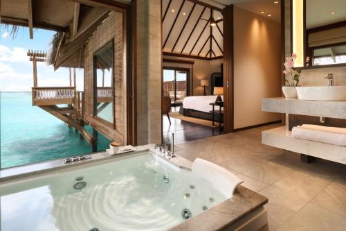 a bathroom with a bath tub and a bedroom at Conrad Maldives Rangali Island in Mandhoo
