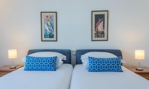 two beds with blue pillows in a bedroom with two lamps at Hotel Adonis in Mýkonos City