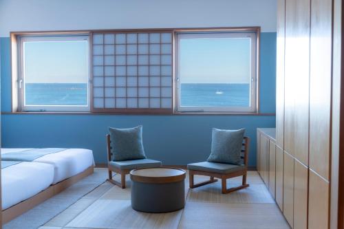 a room with a bed and two chairs and two windows at Hayama Umino Hotel in Hayama