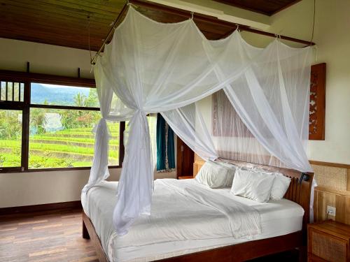a bedroom with a white canopy bed with a window at Lesong Hotel and Restaurant in Munduk