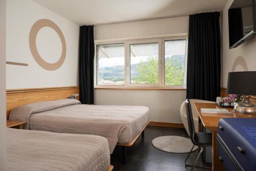 a hotel room with two beds and a desk and window at Hotel Europa Belluno in Belluno