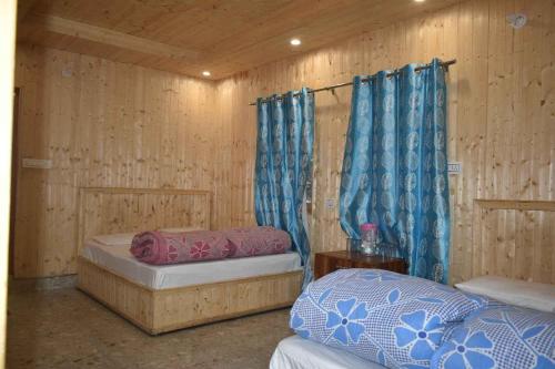 two beds in a room with wooden walls and blue curtains at Devdaar Cottage Gangotri in Gangotri