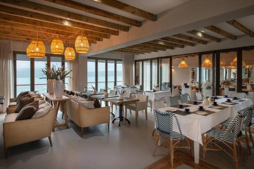 a restaurant with white tables and chairs and windows at The Shark Bay Boutique Hotel & Spa in Langebaan