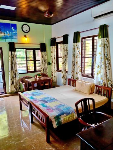 a bedroom with a bed and a table and windows at Cherys Bunglow Homestay- Rooms in Thiruvalla