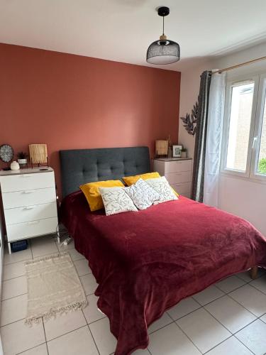 a bedroom with a bed with a red blanket and yellow pillows at La Fleur des Marais - Maison tout confort au calme, grand jardin & balançoire in Le Château-dʼOléron