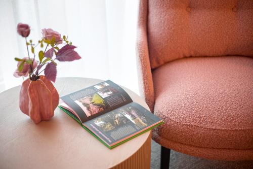 Ein Buch auf einem Tisch neben einem Stuhl mit einer Vase in der Unterkunft Van der Valk Hotel Eindhoven in Eindhoven