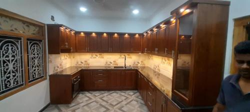 a large kitchen with wooden cabinets and a man standing in it at Europenvilla in Mannar