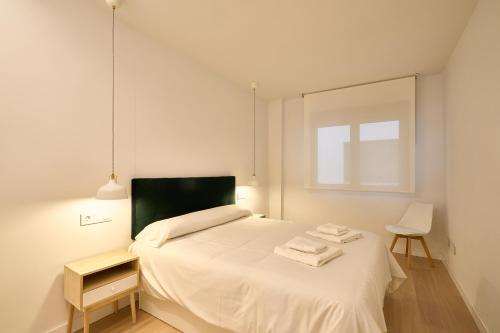a white bedroom with a bed and a chair at Las villas de Manuel in Salamanca