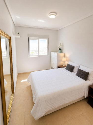 a white bedroom with a large bed and a mirror at La Riviera Residence in Rojales