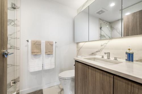 a white bathroom with a toilet and a sink at Bright & Cozy 1BR Steps to Brentwood mall in Burnaby