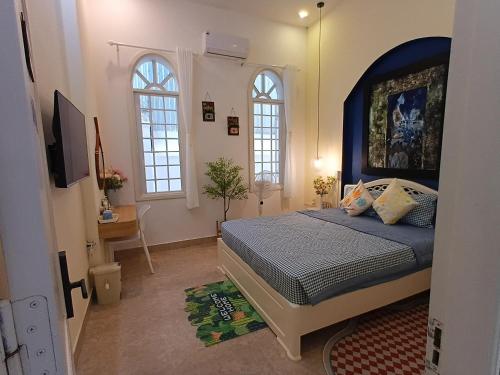 a bedroom with a bed with a blue headboard and two windows at Green hill side Villa in Cồn Giả Viên