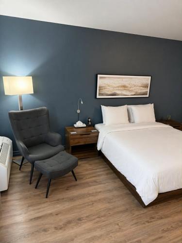 a bedroom with a large bed and a chair at Hôtel Normandie in Rimouski