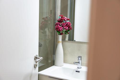 a bathroom sink with a white vase with pink flowers in it at Mourisco Guest House in Alijó