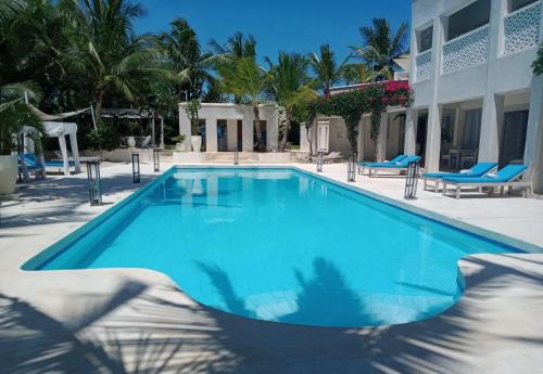a large blue swimming pool with blue chairs and palm trees at The Villa Luxury Suites Hotel in Diani Beach