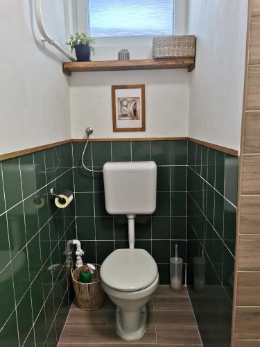 a green tiled bathroom with a toilet and a window at Sára Vendégház in Szentes