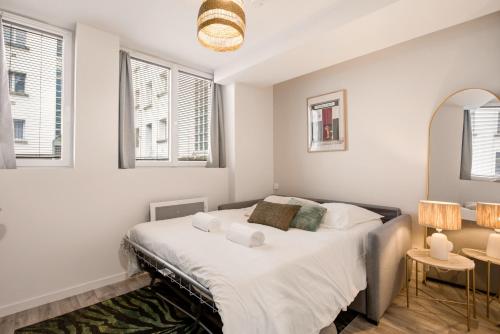 a bedroom with a bed with white sheets and windows at Studio L'Émeraude - F1 lumineux, hypercentre - CAEN in Caen