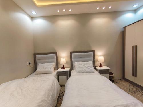 two beds in a room with two tables and two lamps at شقق ضوء القمر Moonlight Apartment in Rahwat al Barr