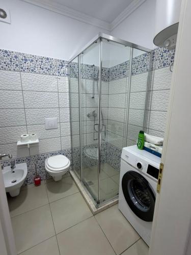 a bathroom with a shower and a toilet and a washing machine at Sun Holiday Apartment in Lezhë