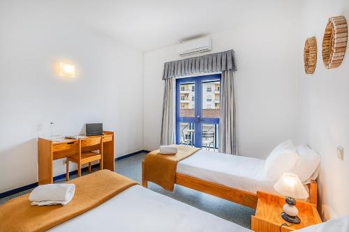 a bedroom with two beds and a desk and a window at HI Beja - Pousada de Juventude in Beja