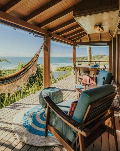 a porch with chairs and a hammock and the ocean at Villa Gardena Suites in Praia do Rosa