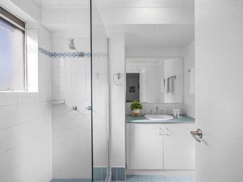 a white bathroom with a shower and a sink at Surfcomber on the Beach in Maroochydore