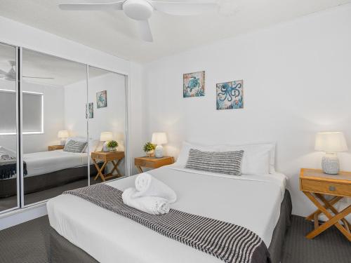 a white bedroom with two beds and a mirror at Surfcomber on the Beach in Maroochydore