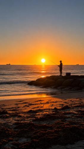 a man fishing on the beach at sunset at Sunset Beach Holiday Park in Geraldton
