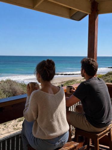 a man and woman sitting on a porch looking out at the beach at Sunset Beach Holiday Park in Geraldton